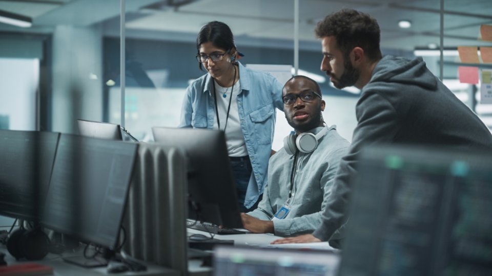 Diverse Multi-Ethnic Team in Modern Office: Teamwork of IT Programmers Gather Around Desktop Computer, Talking, Finding Solution. Specialists Create Software. Engineers Develop App, Program